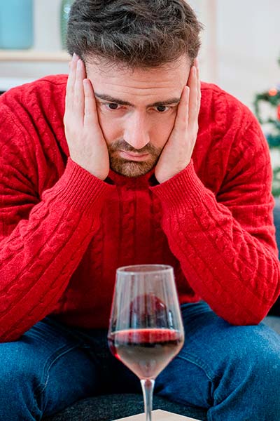 грустный мужчина сидит на диване с бокалом вина