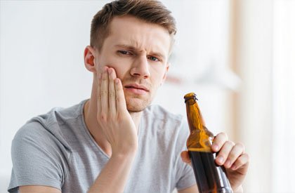 Мужчина держится одной рукой за щёку и пьёт пиво