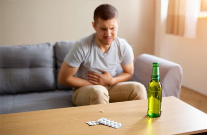 Мужчина сидит на диване и держится руками за живот